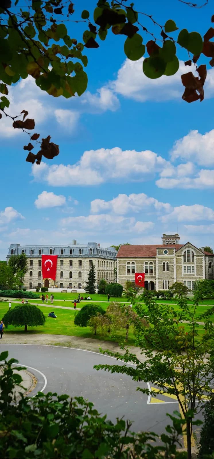Dallar arasından görünen kampüs binaları ve Türk bayrakları, yeşil çimenlik
