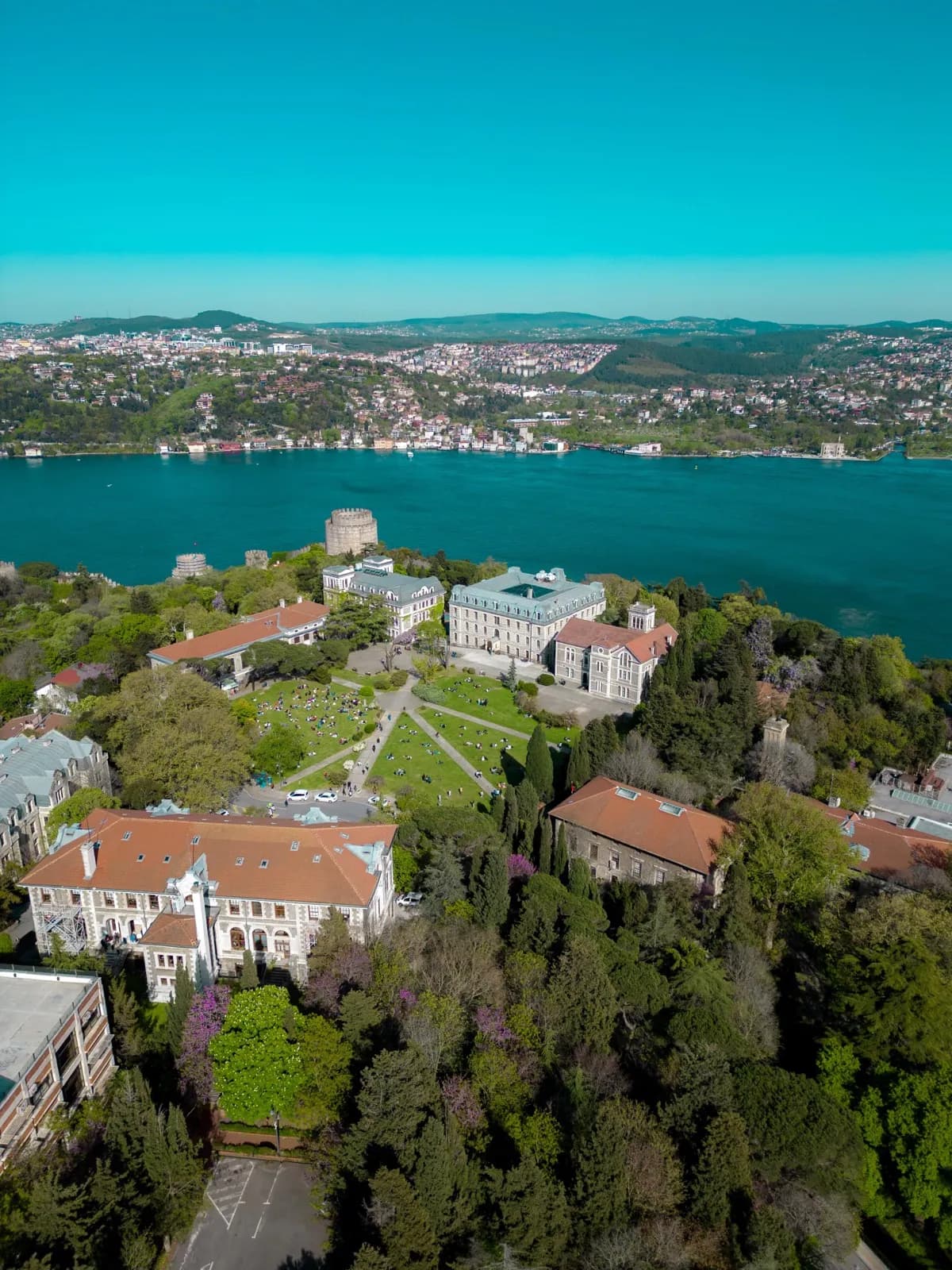 Boğaz'a bakan kampüs kulesi ve yeşil yerleşke, canlı mavi sularla kuş bakışı